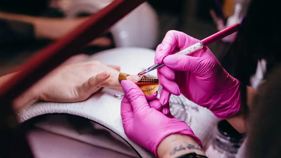 Nail technician in pink gloves painting a client's nails