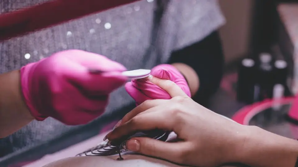 Gloved nail technician filing a client's nails